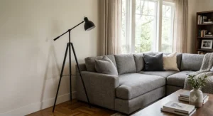 Matte black adjustable tripod standing lamp placed in the corner behind a modern gray sectional sofa